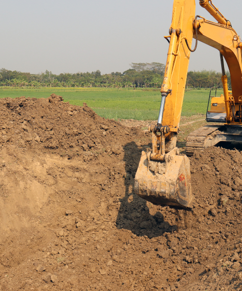 A yellow excavator digging dirt in a field